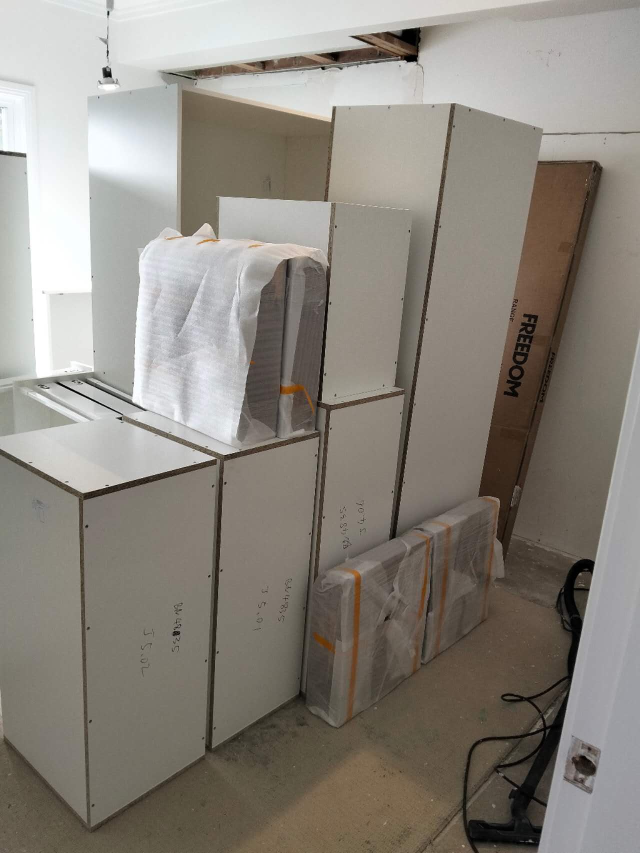 White kitchen cabinet frames and flat-packed boxes stacked in a room during home renovation.
