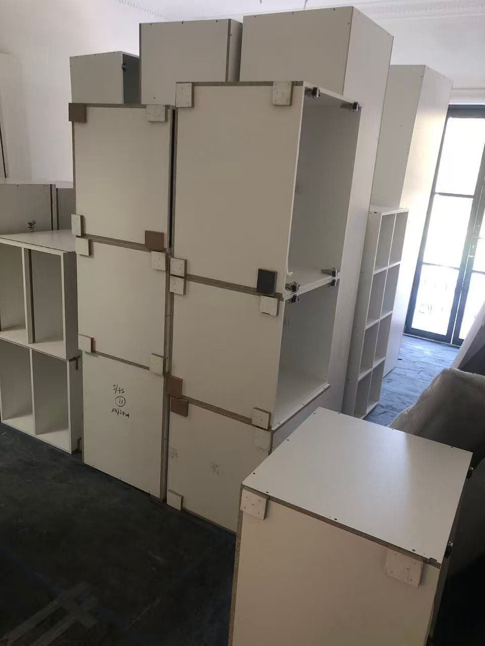 White modular kitchen cabinet units stacked high in a room, awaiting assembly and installation.