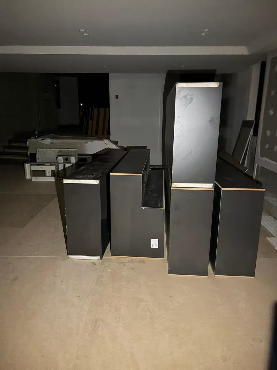 Multiple black rectangular storage units stand in a dimly lit room with unfinished concrete floors.