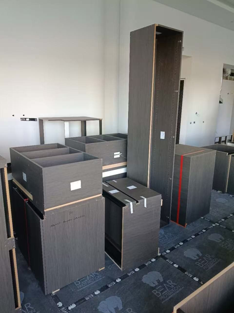 Dark grey wood-textured cabinet carcasses and a tall pantry unit during a kitchen installation.