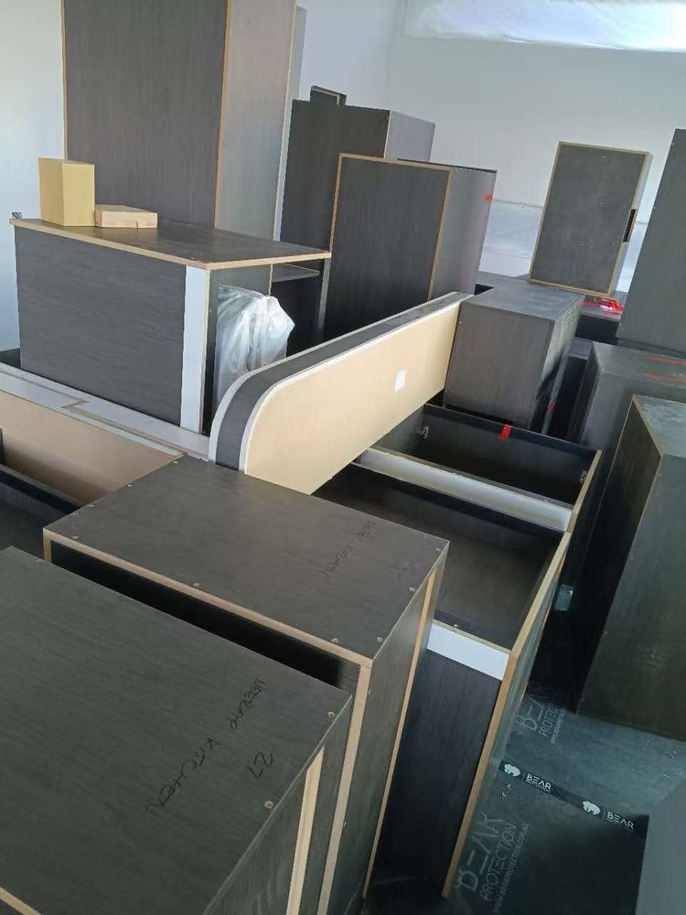 Dark wood-grain kitchen cabinets and components stacked in a room for assembly and installation.
