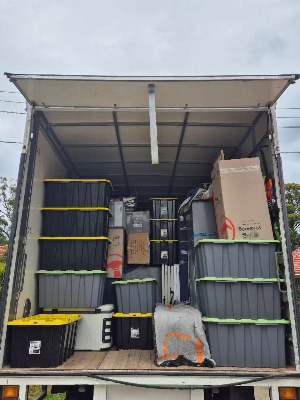 Stacks of black and grey plastic storage bins and cardboard boxes inside a moving truck.