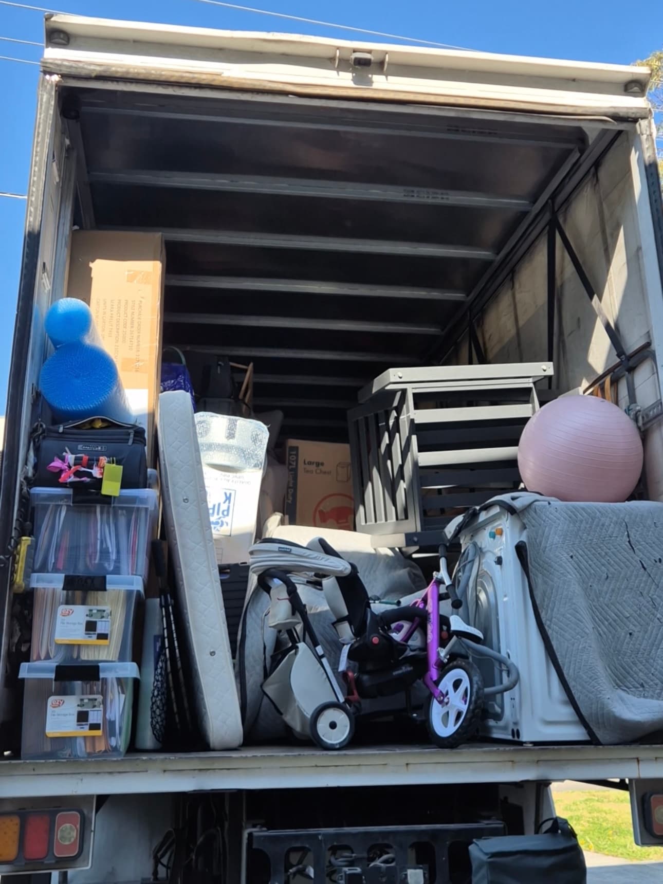 Moving truck interior packed with household items including a stroller, washing machine, and storage bins.