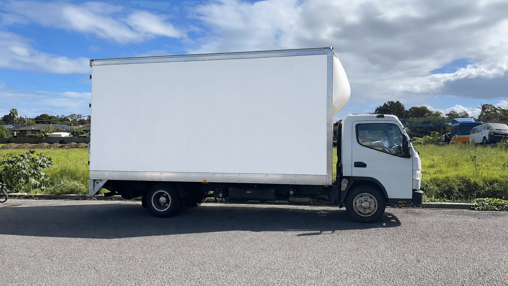 White box truck parked on a road beside a grassy field under a cloudy sky.