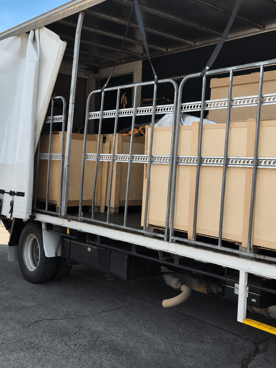 Large wooden crates secured behind metal railings inside an open-sided delivery truck.